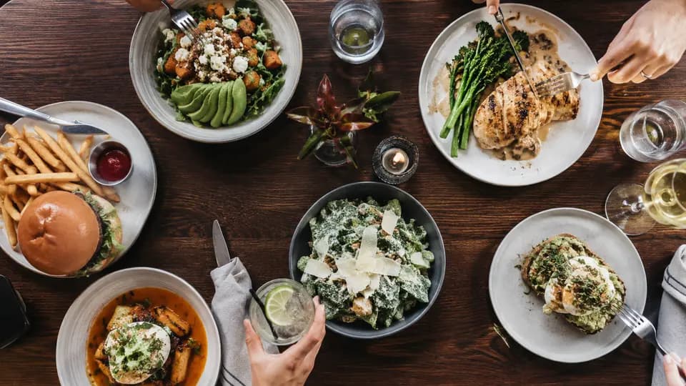 A restaurant table with a balanced meal, water glass, menu, and phone for mindful meal tracking